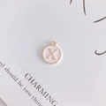 Detail shot of a round pink enamel pendant with gold letter X for DIY jewelry - Letter X