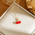 Detail of gold cherry pendant necklace with red beads and crystal leaves on jewelry box - Gold Cherry