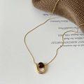 Detail van tijgeroog hanger aan gouden ketting tegen een gezellige gebreide achtergrond - Goud