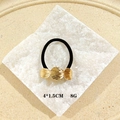 Black ponytail holder with three golden shell accents on a textured stone block - Brushed Leaves