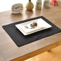 Black rectangular linen placemat on a wooden table with ceramic plate and cutlery - Black