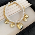 Dettaglio collana a due strati con perle e pendenti a cuore dorati su vassoio beige - Oro