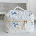 Detalle de neceser acolchado blanco con lunares azules y un diseño de lazo azul suave - Neceser de mano