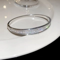 Detailopname van een zilveren open armband met glanzende zirkonia op wit porselein - Volledig Diamanten Ronde Stijl (Yuanxing) / Zilver
