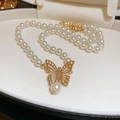 Collar de perlas multicapa con colgante de mariposa dorada sobre un cojín de color beige - Estilo de Perla con Colgante de Mariposa Dorada