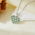 Macro detail of silver heart pendant with green zircon stones on silk fabric - Steel Color Heart Green Zircon Hollow Necklace (T021)