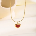 Collar de acero de titanio dorado con colgante de corazón rojo sobre tela crema - Collar