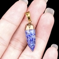 Lapis lazuli stone cone pendant with gold metal clasp held in hand on black background - Lapis Lazuli