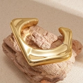 Makro-Detail von hochglanzpoliertem Gold-Armreif in unregelmäßiger Geometrie auf Stein - Gold