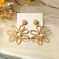 Detailed close-up of woven raffia flower earrings with a hollow-out summer vacation design - Brown