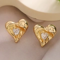 Detalle macro de pendientes de corazón dorados con circón brillante y textura única - Forma de Corazón Irregular / Dorado
