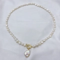 Dettaglio collana di perle barocche con chiusura a T dorata su tessuto di seta bianco - Stile Barocco
