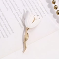 Vista dettagliata di un'elegante spilla a tulipano bianco con foglie dorate su libro vintage - Stile Tulipano Bianco