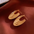 Detailed view of gold C-shaped earrings with layered ridges on red silk fabric - Gold