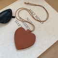 Detail of a brown leather heart-shaped charm featuring fine stitching and pebble texture - Coffee