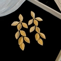 Detalle macro de pendientes de hoja dorada con textura de nervaduras sobre fondo negro - Estilo de Borla de Hoja de Pin de Plata / Dorado