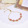 Macro detail of gold adjustable bracelet featuring enamel evil eye heart charms and zircons - Red