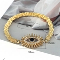 Goldenes Perlenarmband mit Evil Eye Anhänger und Kristalldetails auf grauem Stoff - Gold