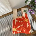 Top-down view of knitted tote bag with orange floral patterns on a glass surface - Kapok Flower Orange Beige