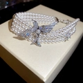 Makroaufnahme eines mehrlagigen Perlenarmbands mit Zirkonia-Vogel und Stern-Anhänger - Silber-Weiß