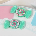 Detailed macro view of two green resin candy-shaped charms with colorful spiral patterns - Teal