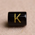 Macro shot of a black rectangular bead with a gold-stamped letter K for DIY jewelry - Letter K
