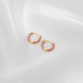 Macro view of gold hoop earrings with red enamel detail on a white silk background - Fuschia