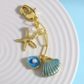 Llavero con estrella de mar dorada y colgante de concha azul con perlas en plato blanco - Azul