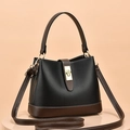 Bolso saco de cuero negro y marrón con hebilla dorada sobre pedestal neutro - Negro