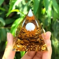 Orgonite pyramid with tiger eye stones, gold foil, and lotus charm held in hand - Tiger Eye and Golden Lotus (44) / 5cm