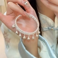 Detail of silver bell tassel bracelet with woven texture on a model wearing a cheongsam - Silver