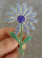 Broche fleur dorée aux pétales bleu clair et strass bleu foncé tenue à la main - Fleur en Strass Bleu-Vert