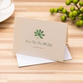 Beige textured greeting card with green leaves and white envelope on wooden desk - Love You For All Life / With Envelope