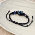 Close-up of black braided bracelet with blue-eyed cat charm on a ceramic plate - Blue Cat
