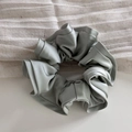 Macro detail of glossy sage green satin scrunchie with elegant ruffled texture - Light Green