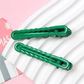 Macro shot of two green metal hair clips with wavy texture on a white tray - Green