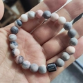 Pink and grey natural stone bead bracelet held in hand featuring a black cylinder charm - Pink Zebra Stone