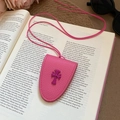 Close-up of pink leather glasses holder necklace with purple cross detail on an open book - Rose Red