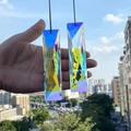 Macro shot of two long K9 crystal suncatcher prisms with rainbow coating held against sky - Faceted Long Strip 120mm