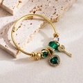 Macro shot of gold spiral bangle with green heart gemstone and crown charms on stone - Green