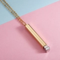 Close-up of golden vertical bar pendant with silver cube detail on two-tone background - Steel Inner + Gold Outer