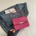 Pink V-quilted faux leather crossbody bag with gold chain strap held against blue denim - Rose Pink
