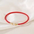 Detailed close-up of a red woven bracelet with gold metal end caps on white silk - Red