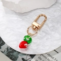 Golden keychain featuring a red strawberry glass pendant with white polka dots - Strawberry
