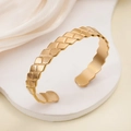 Minimalist golden C-shape bangle with geometric woven texture on white pedestal - Rhombus Woven / Gold