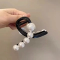 Dettaglio di una molletta nera per capelli con grandi perle bianche tenuta in mano - Nero Lucido