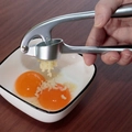 Silver stainless steel manual garlic press squeezing minced garlic into a white bowl - Matte Garlic Press OPP Bag