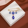 Detail shot of golden safety pin brooch featuring blue evil eye and Hamsa hand charms - Blue Hamsa Style (Z98)