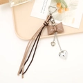 Close-up of a beige leather bow keychain with silver heart charms and fringe tassels - Coffee Bow