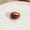 Close-up of amber resin ring with tortoise pattern on a white wavy ceramic dish - Dark Brown Oval